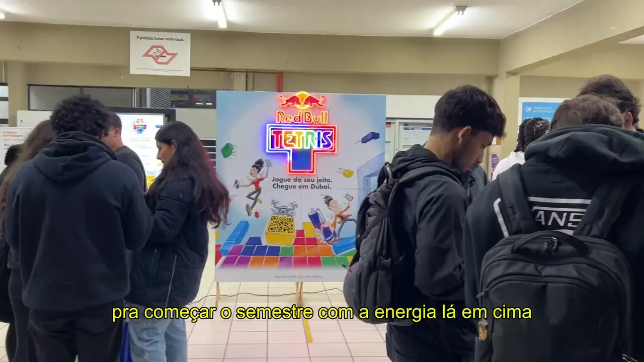 Estudantes reunidos em frente a estande promocional da Red Bull com letreiro 'Tetris' durante recepção no campus.